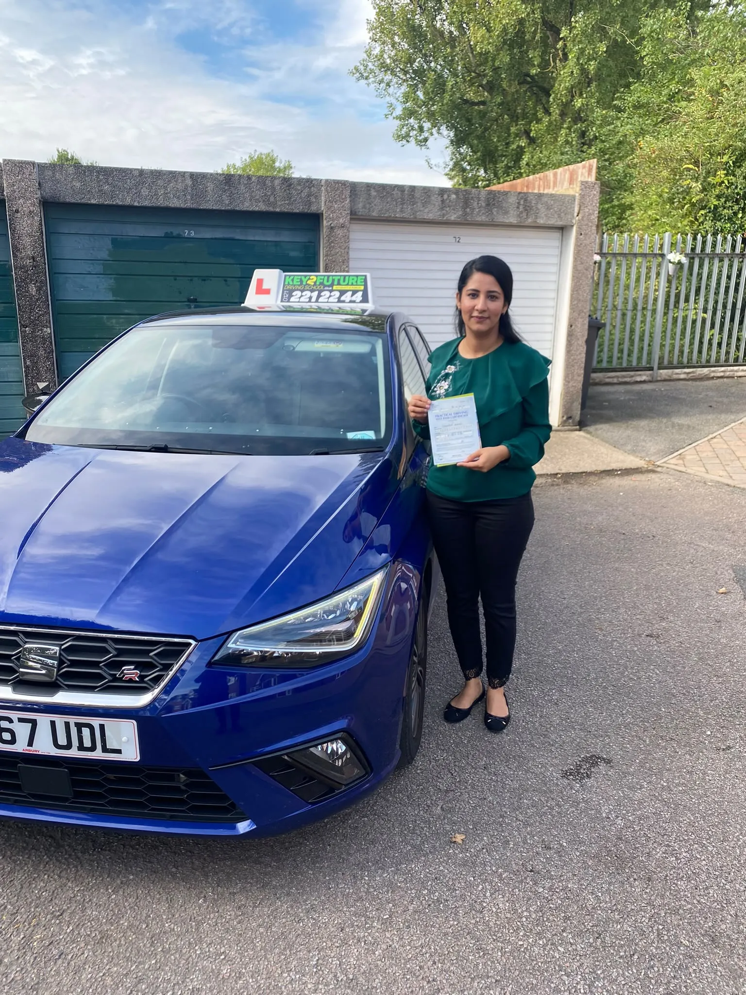 A student holding her driving test pass certificate beside the Key2Future tuition car
