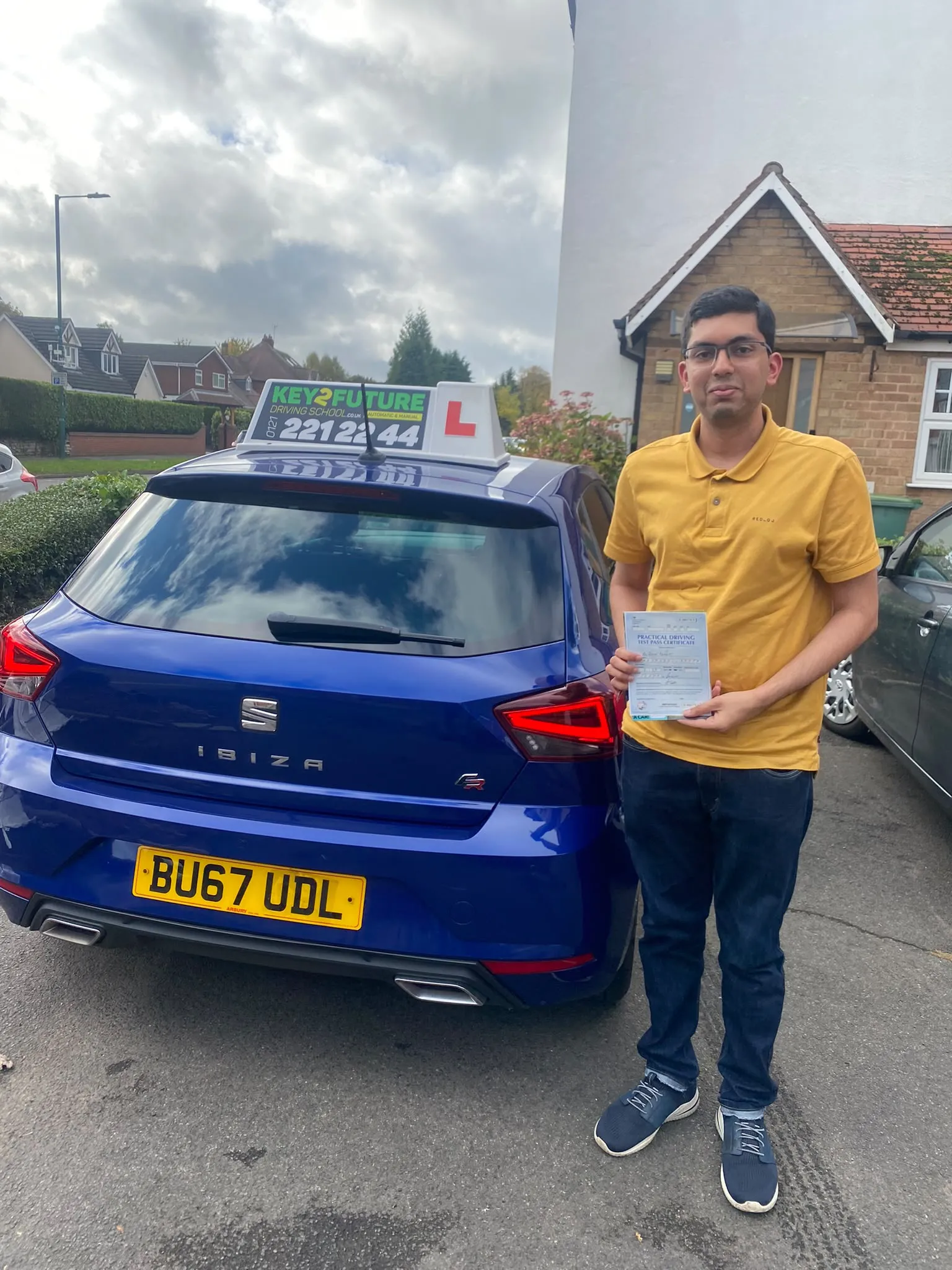 A learner holding his practical driving test pass certificate next to the school's blue car
