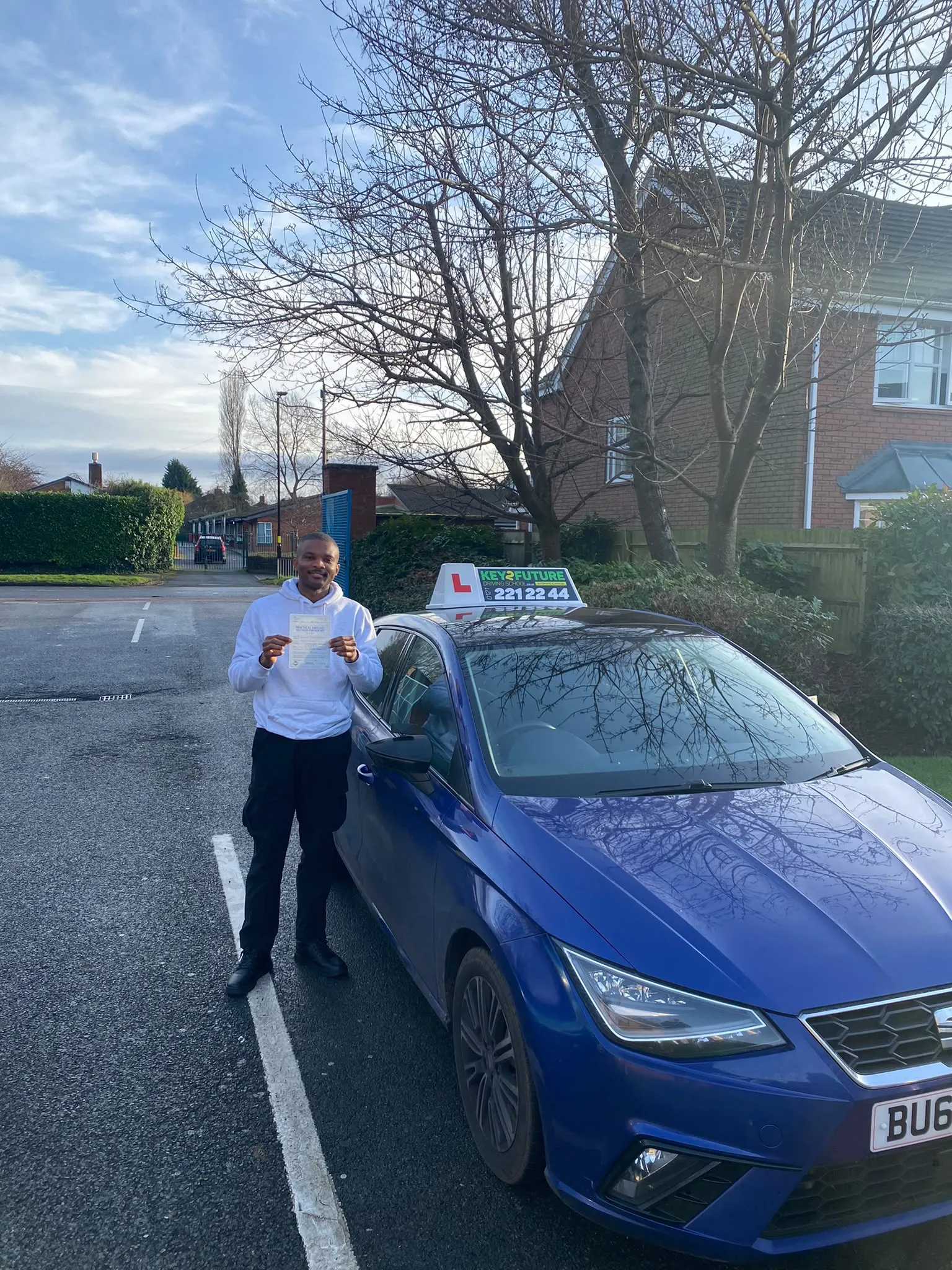 A student holding his pass certificate beside a Key2Future car on a winter morning