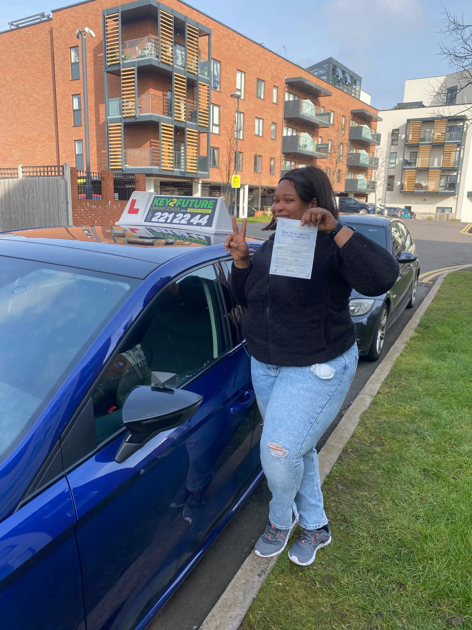 A learner celebrating with her driving test pass certificate beside the Key2Future tuition car